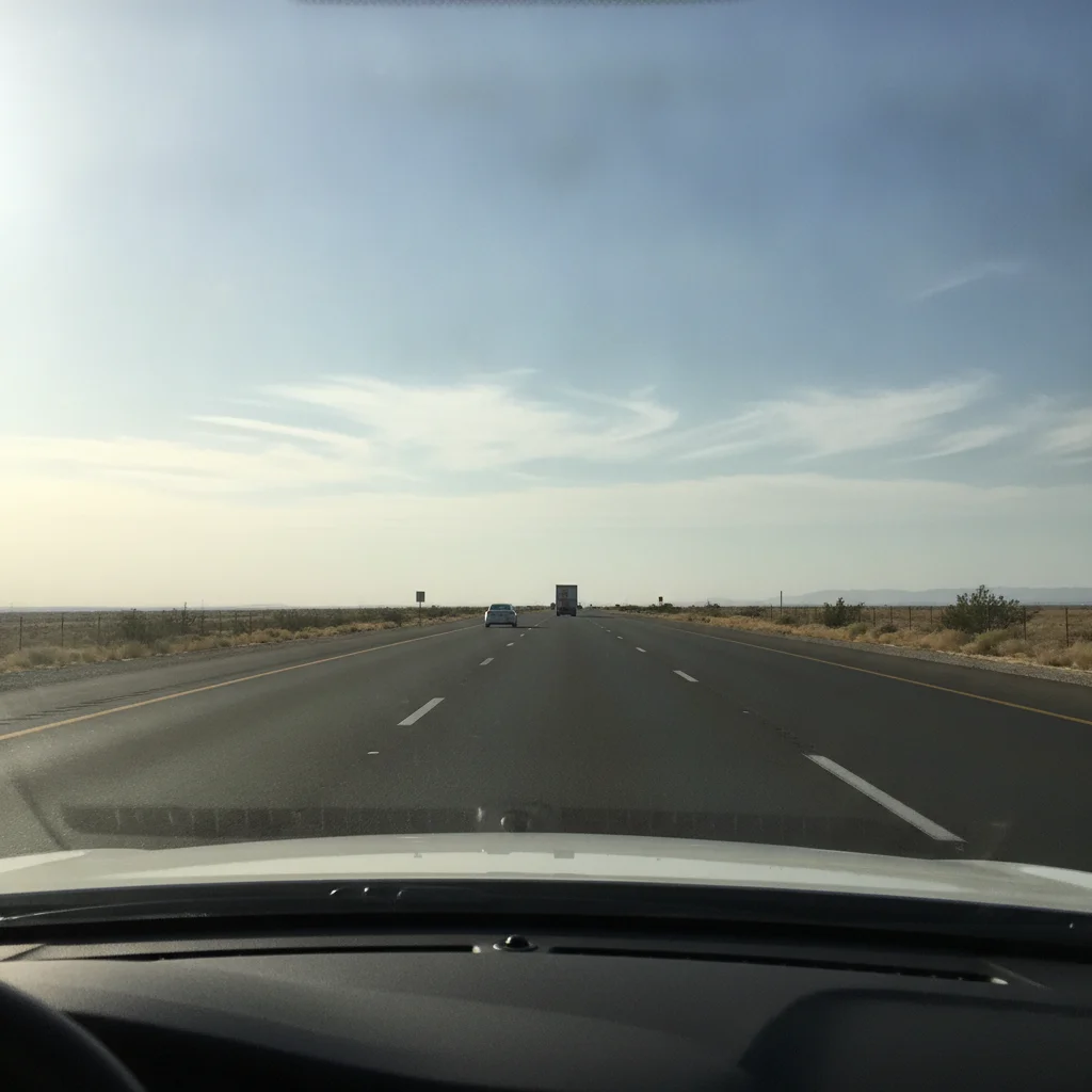 Open flat highway seen from driver's perspective through windshield under clear blue sky